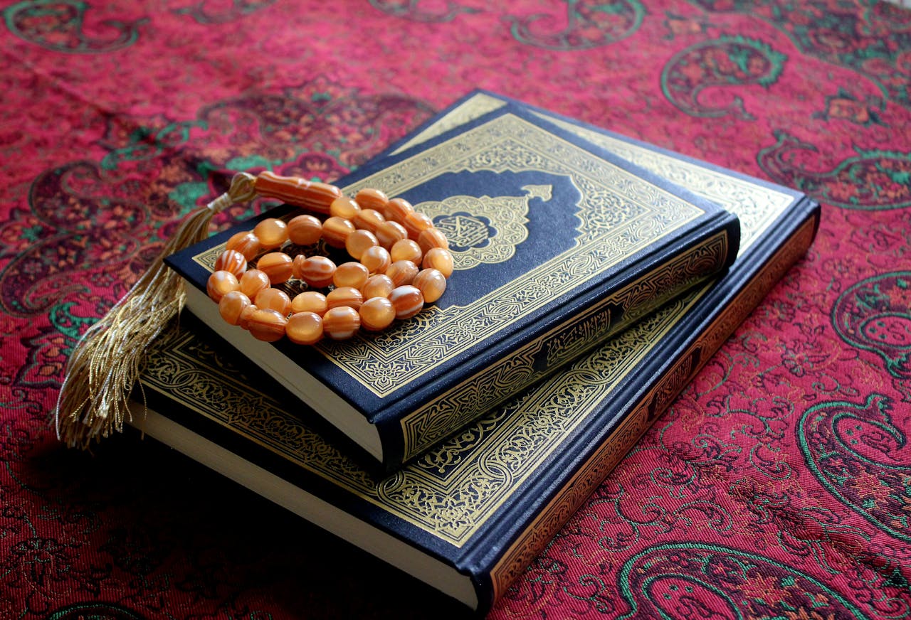An arrangement of the Holy Quran with a Tasbih rosary on a traditional red patterned fabric.