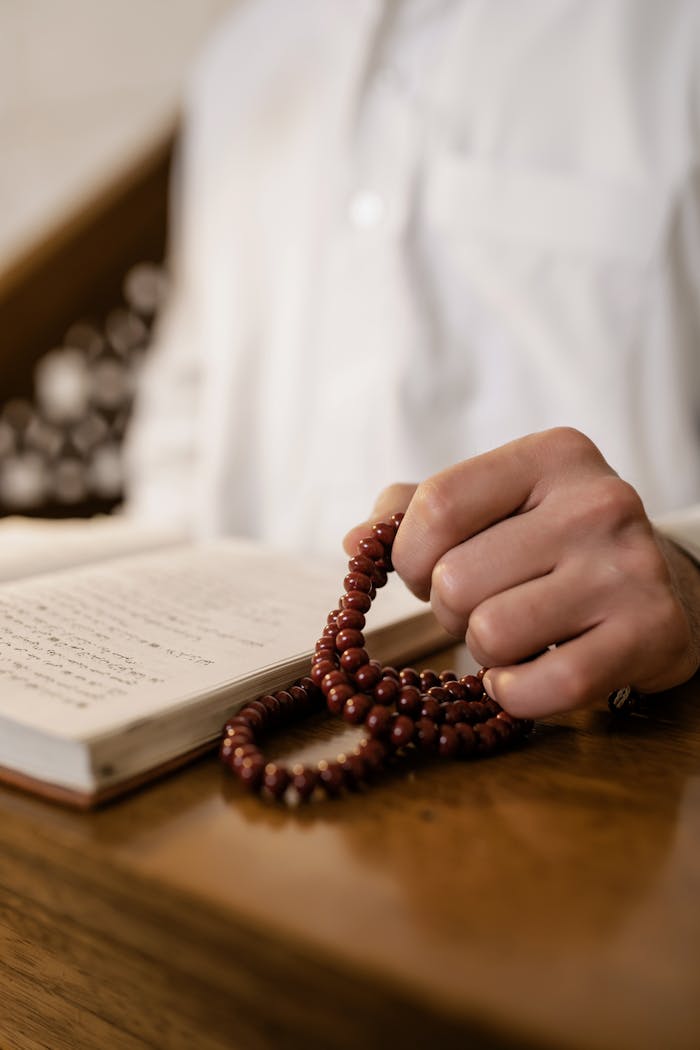 Focused image of a hand holding rosary beads next to an open book, symbolizing faith and reflection.